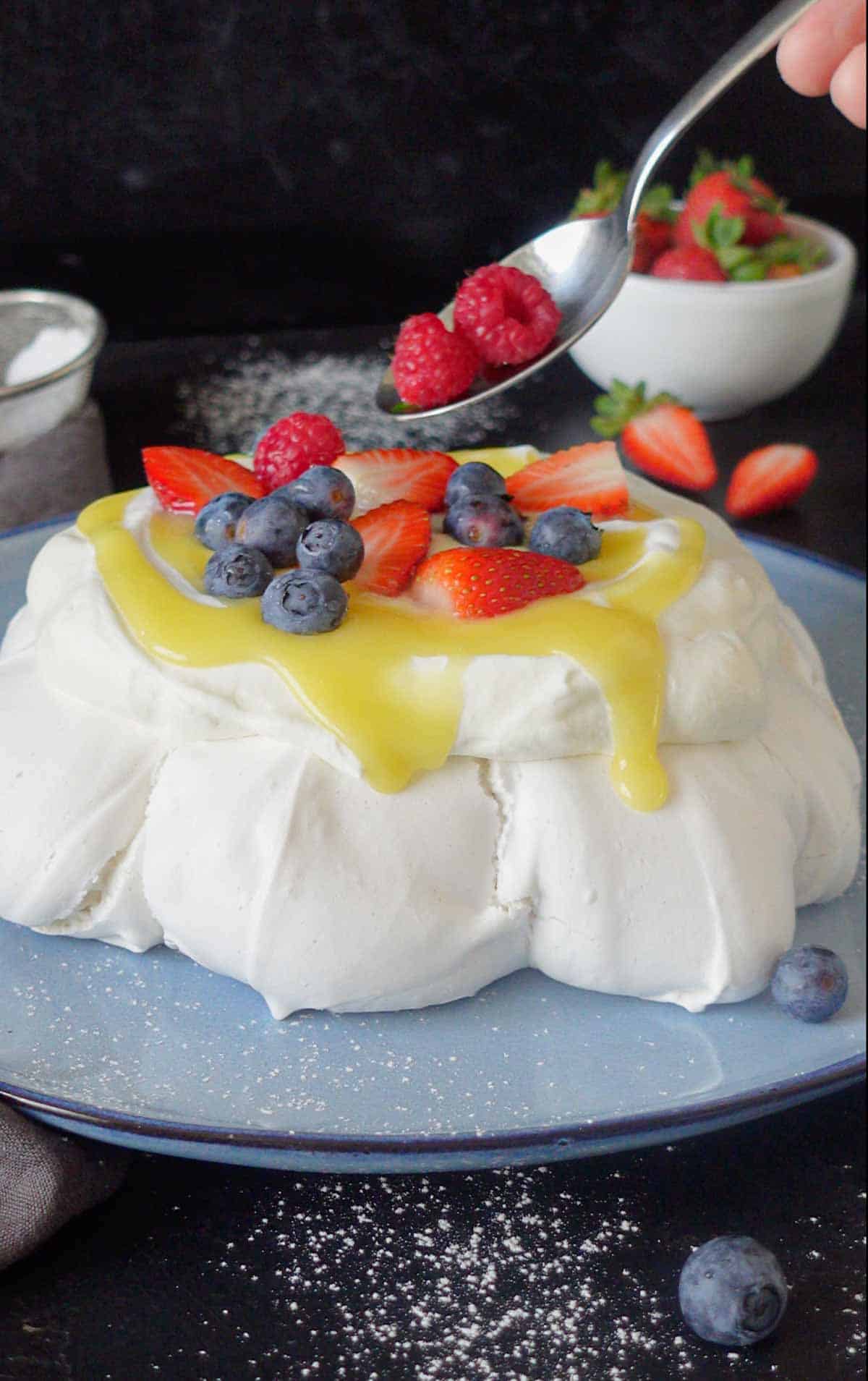 Image: vegan pavlova getting topped with berries