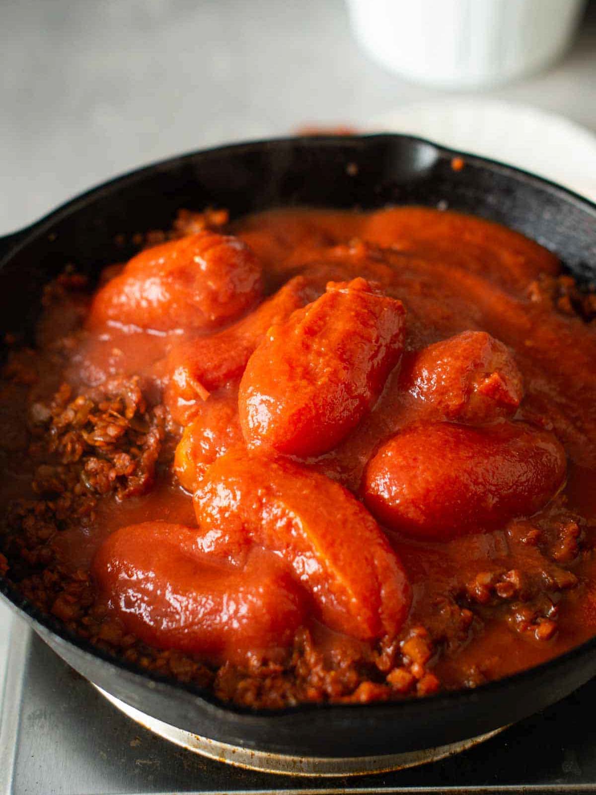 the image shows the tomatoes getting mixed into the vegan lentil bolognese